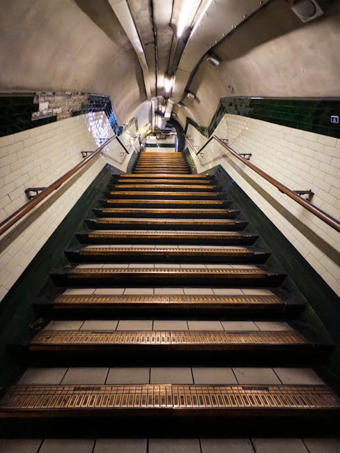 A photograph of an indoor escalator in a modern transport hub or public building, with metal handrails and steps, flanked by smooth, white wall surfaces and a curved concrete section on the left. The