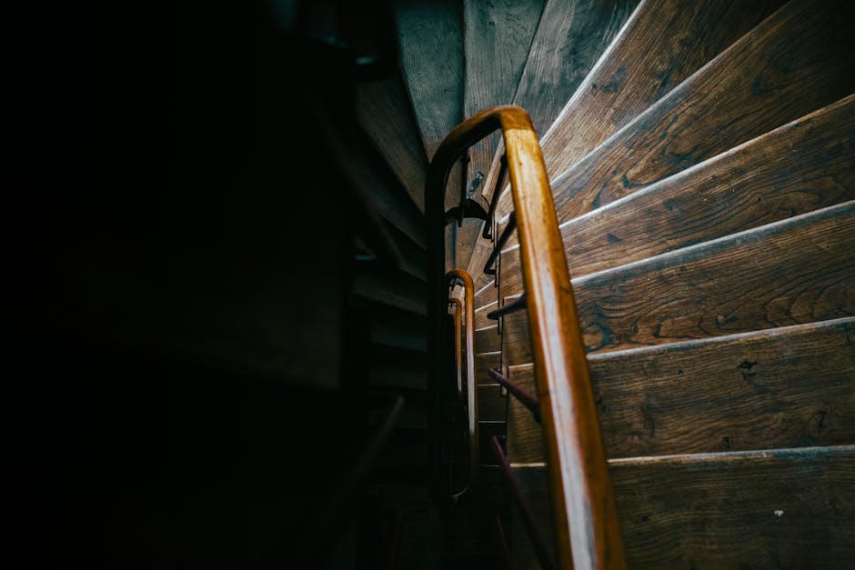 A photograph depicts a narrow outdoor staircase made of weathered concrete steps, ascending between two tall, historic buildings with ornate architectural details and light-colored facades. The stairc